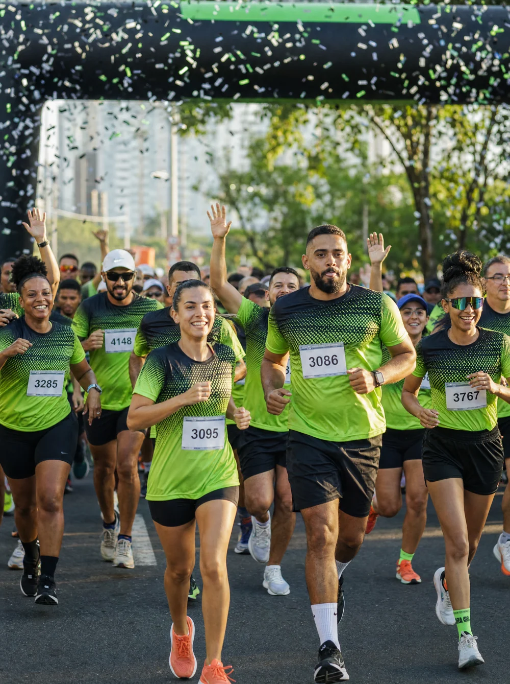 Largada de corrida de rua com multidão de corredores usando a camiseta oficial do evento e número de peito